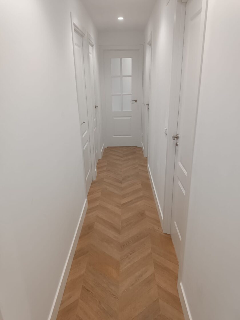 Instalación de tarima flotante con rodapié y puertas blancas.