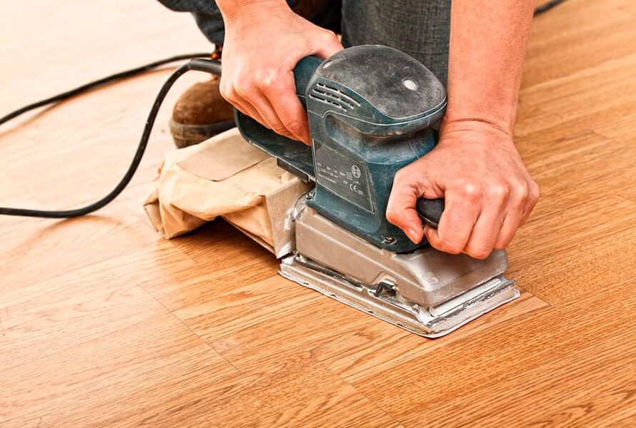 Trabajador lijando un suelo de madera con una lija de mano automática