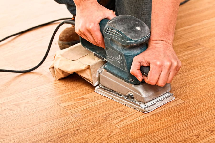 Trabajador lijando un suelo de madera con una lija de mano automática