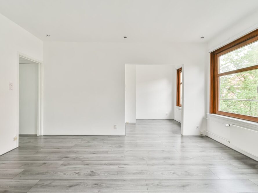 Interior de una habitación con paredes blancas, ventanas al exterior y tarima de color gris en el suelo.